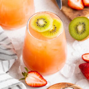 An orange mocktail with kiwi and strawberries on top.