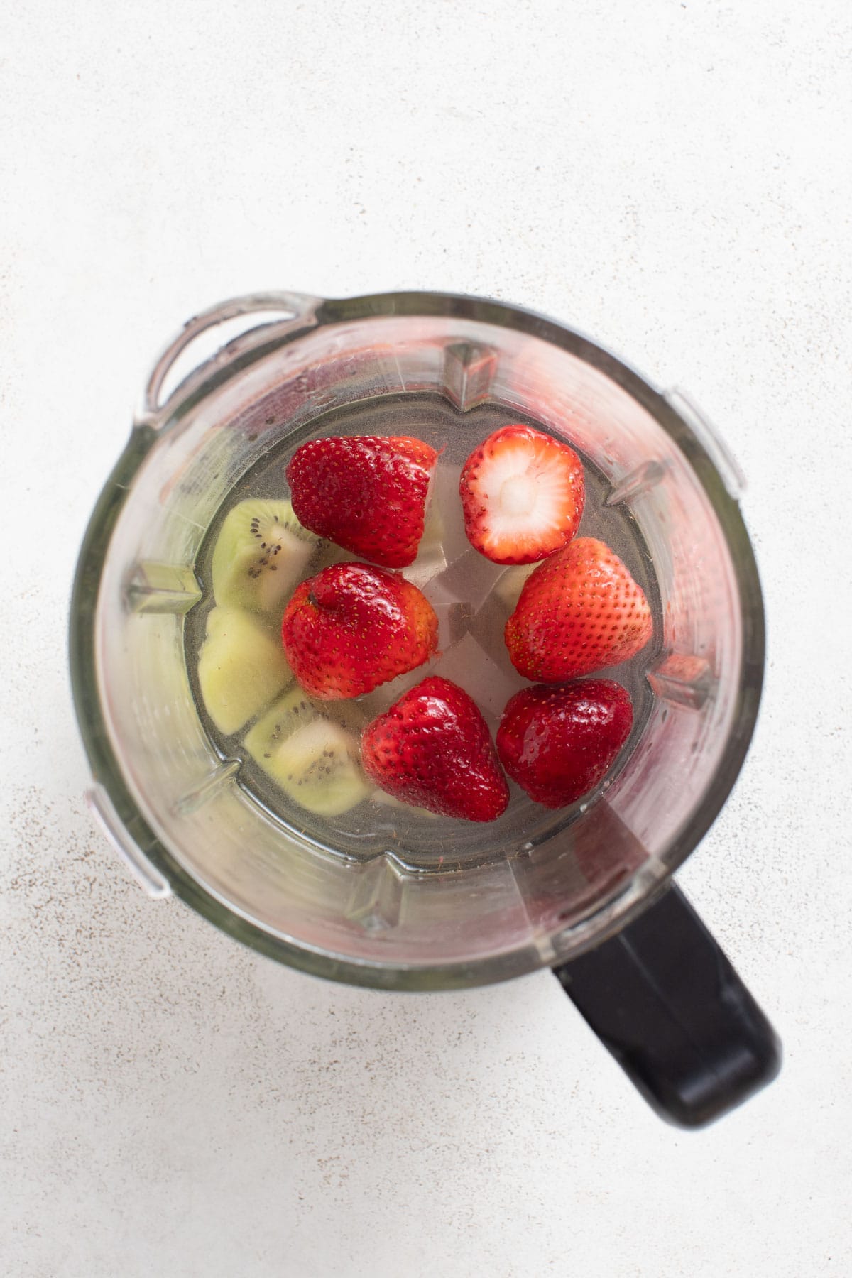 A blender with kiwi and strawberries, and coconut water.