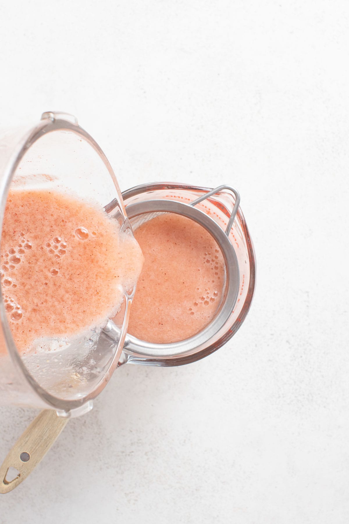 Pouring the mocktail into a strainer to strain out the pulp.