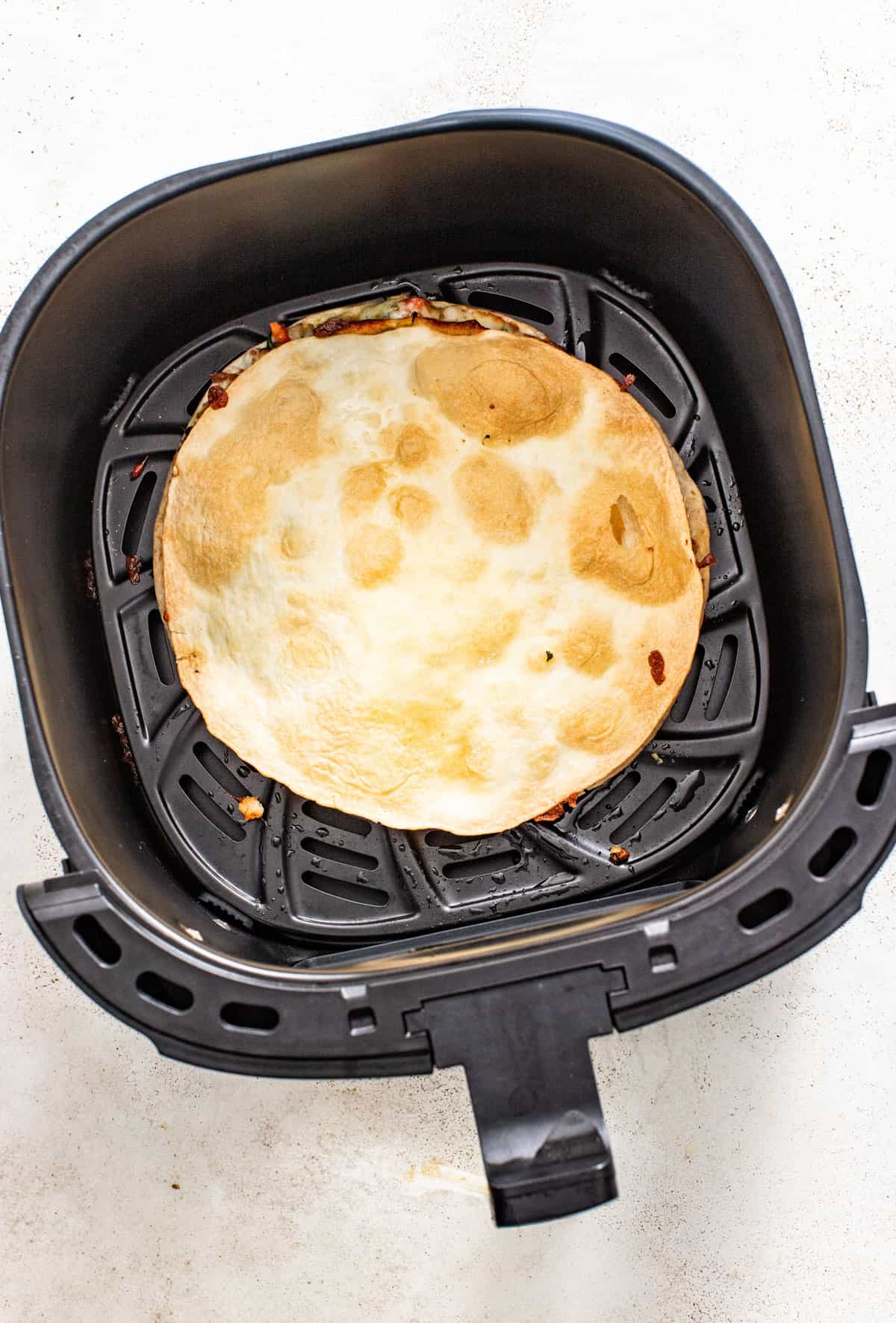 A quesadilla in the air fryer after cooking till crispy.