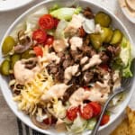 A burger bowl with tomatoes, cheese, and pickles topped with a creamy big mac sauce.