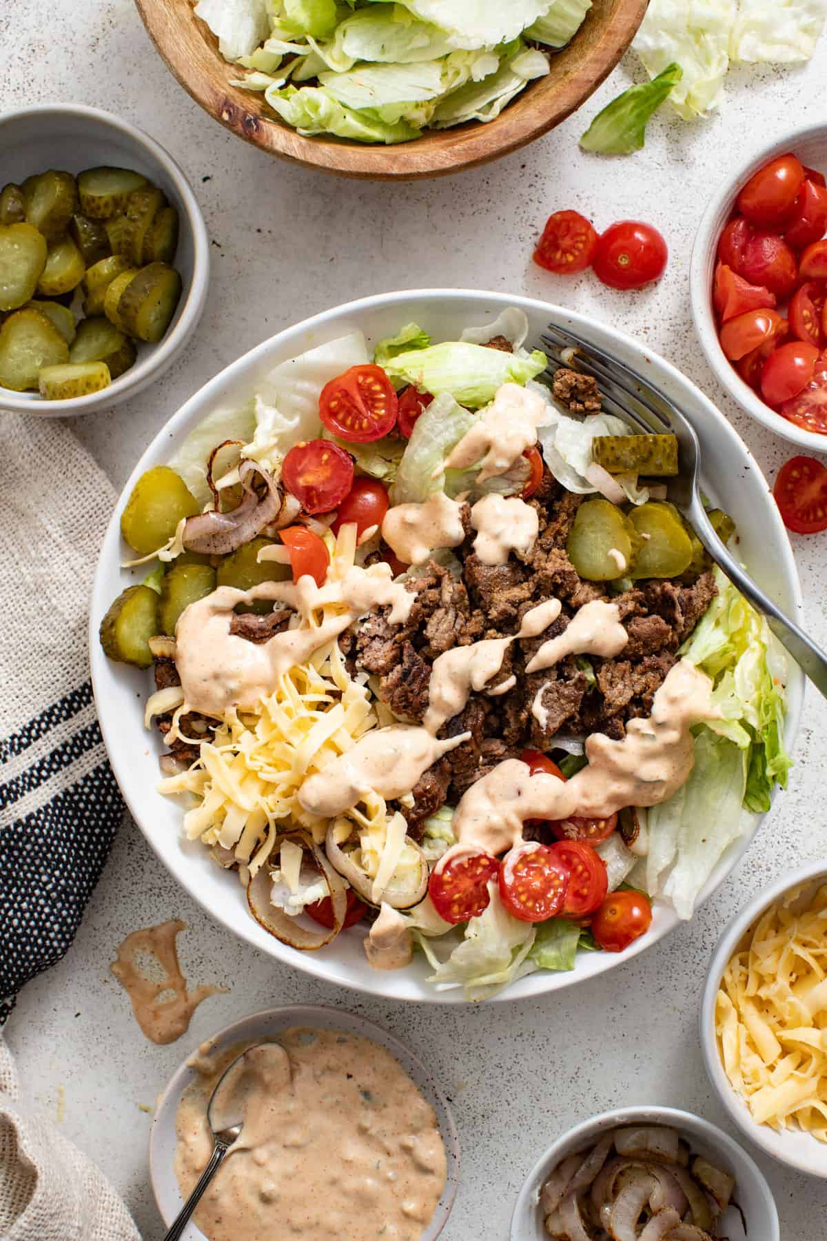 Adding toppings like tomatoes, cheese, and sauce to the burger bowl.