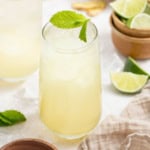 A sparkling drink with coconut water and ginger, topped with mint leaves with cut limes on the side.