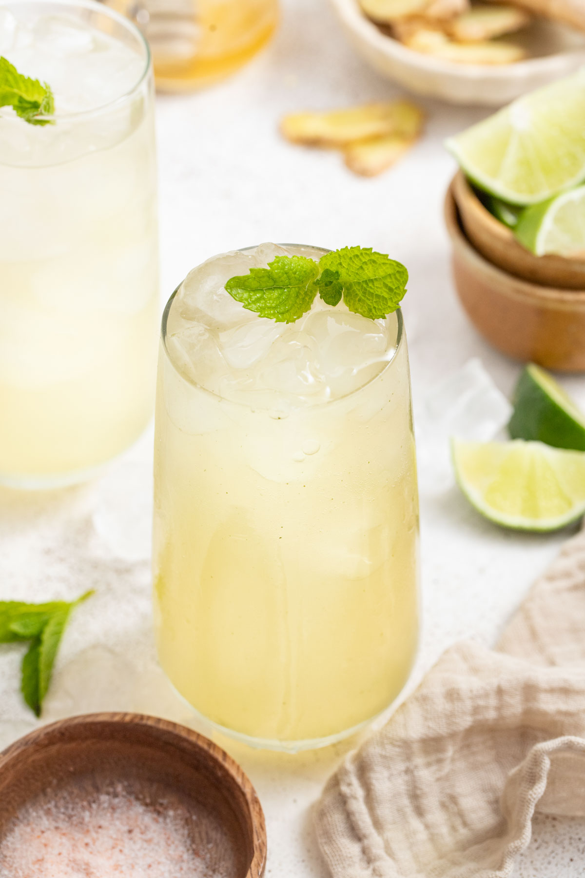 A drink with ginger and fresh mint next to bowls of limes and mineral salt.