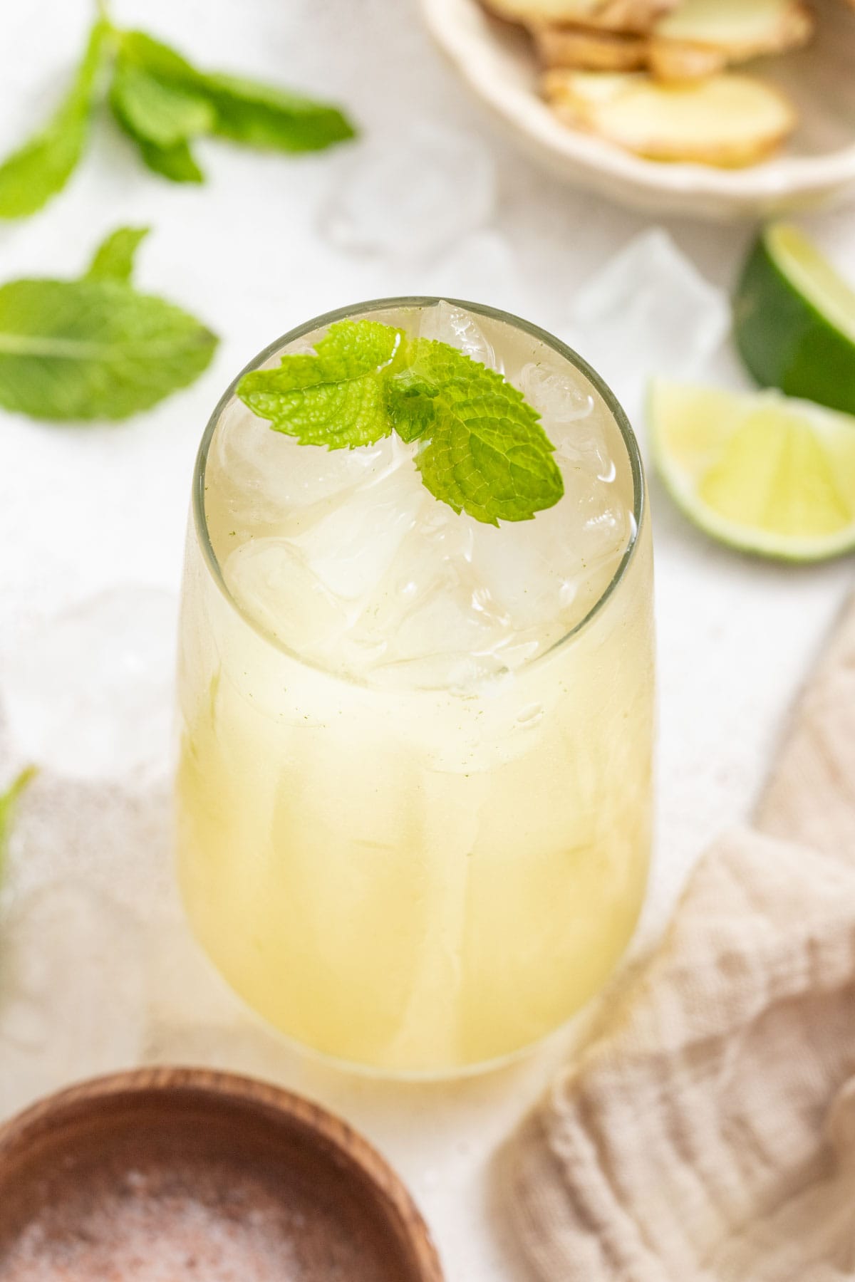 A glass of a ginger drink with mint leaves and a bowl of ginger.