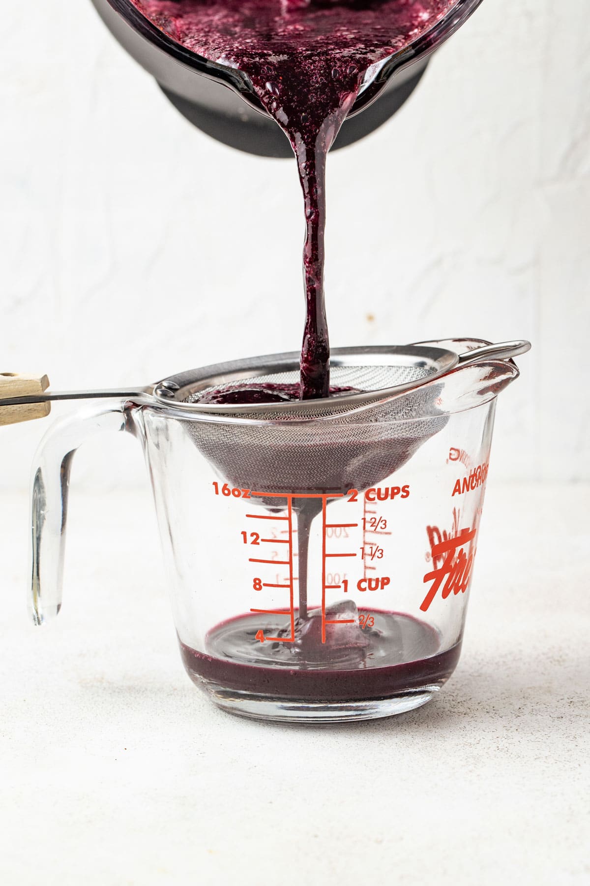 Blueberry mint juice being strained through a fine mesh strainer.