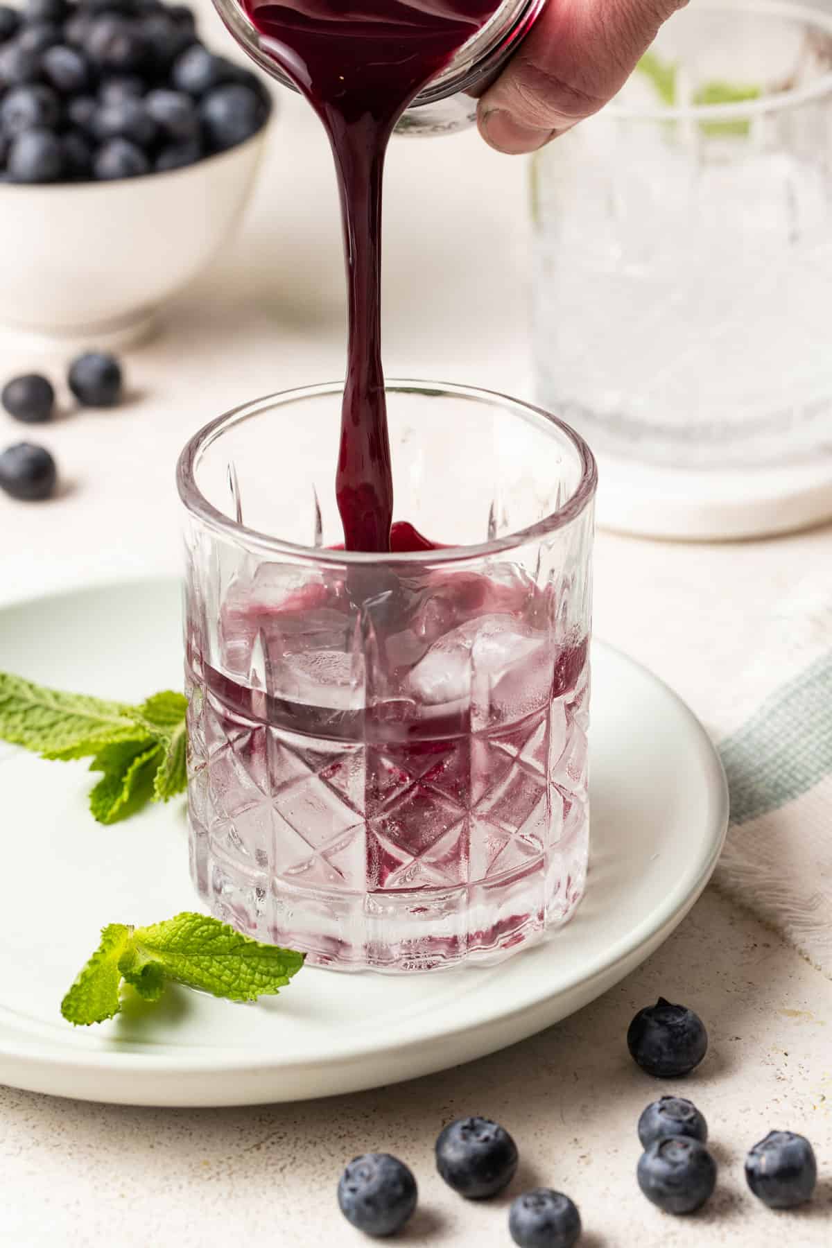 Pouring a blueberry mint syrup into sparkling water.