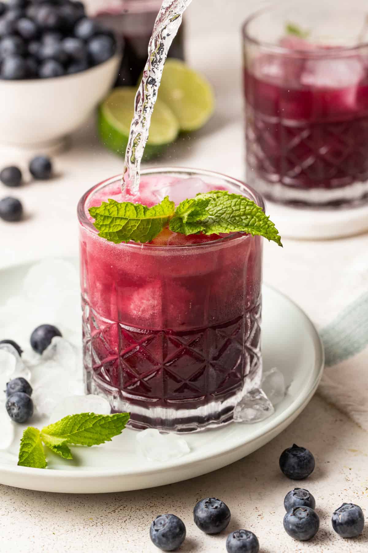 Topping the blueberry mojito with sparkling water.
