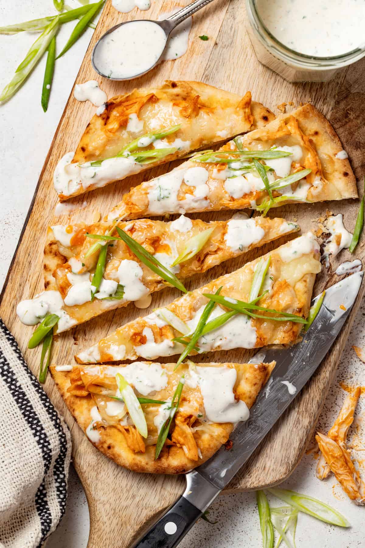 Buffalo chicken flatbread sliced on a cutting board with a knife.