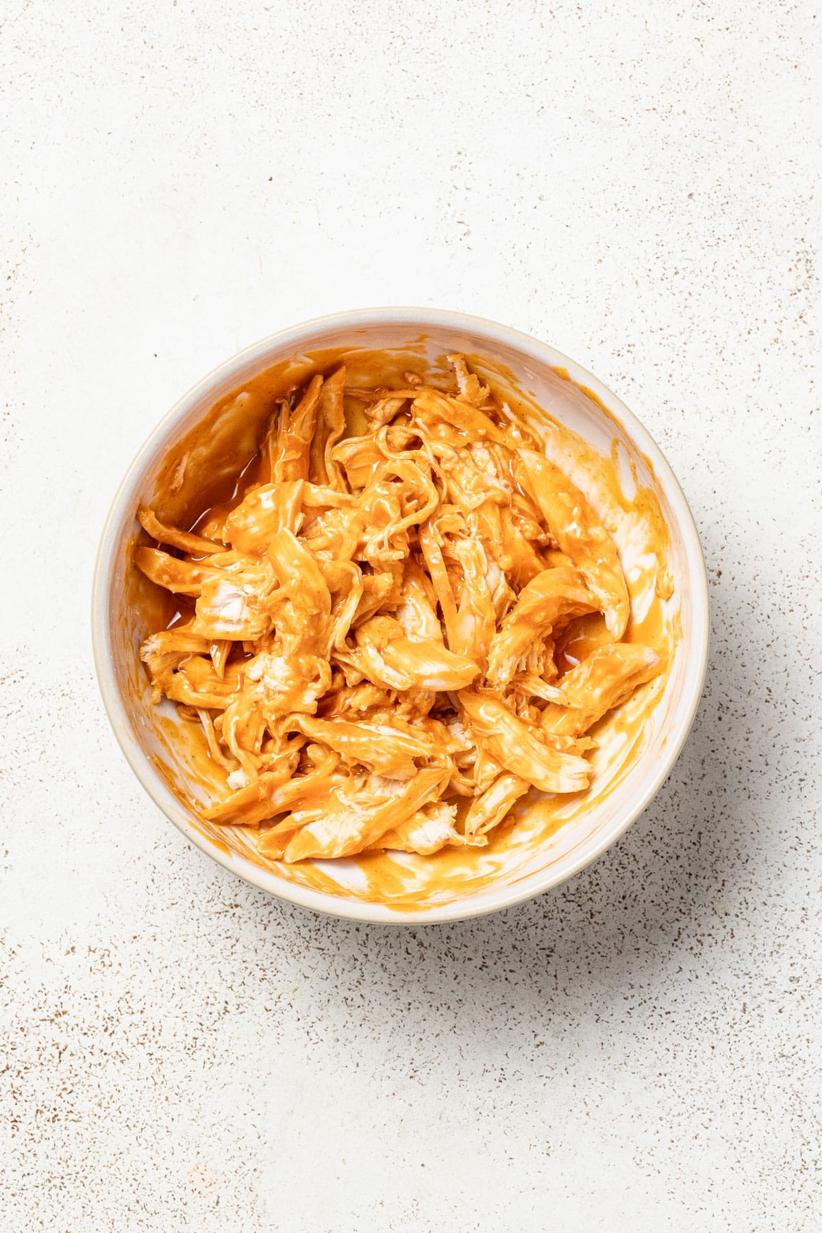 Mixing buffalo sauce and chicken together in a bowl.