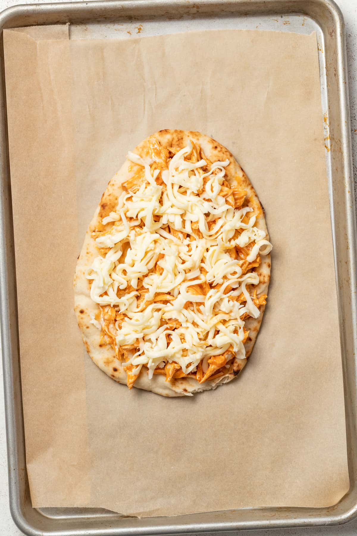 Flatbread topped with buffalo chicken and cheese on a baking tray.