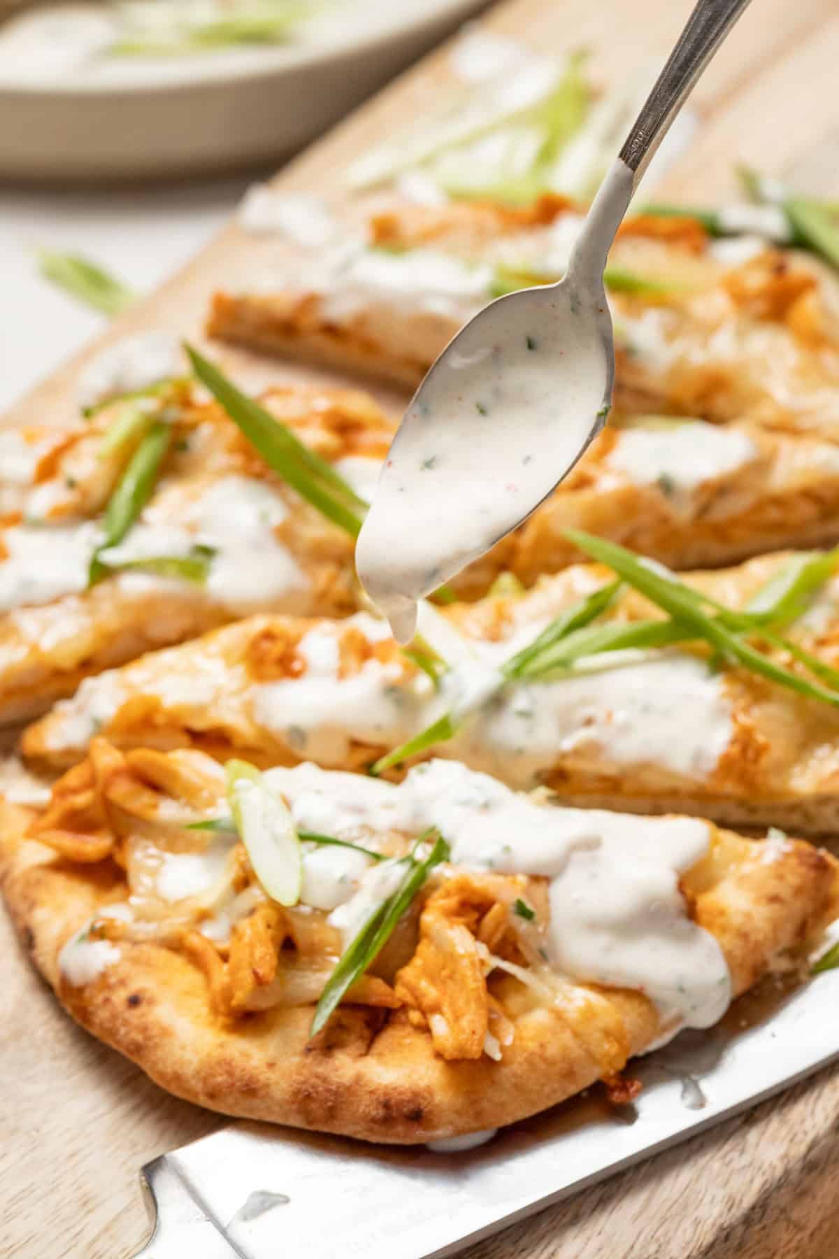 A spoon drizzling ranch dressing on top of the buffalo chicken flatbread.