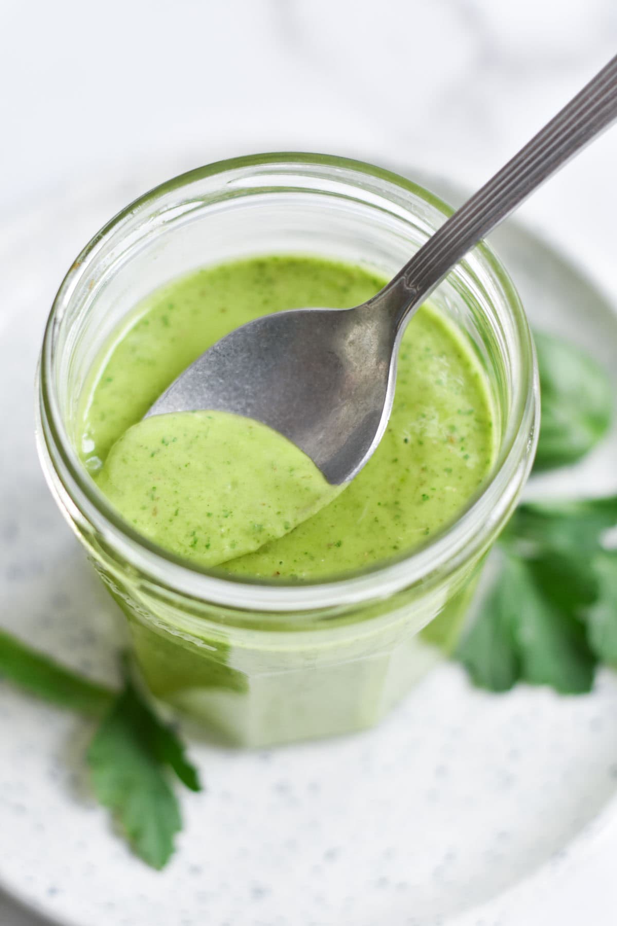 A spoon dipping into a green dressing next to parsley.