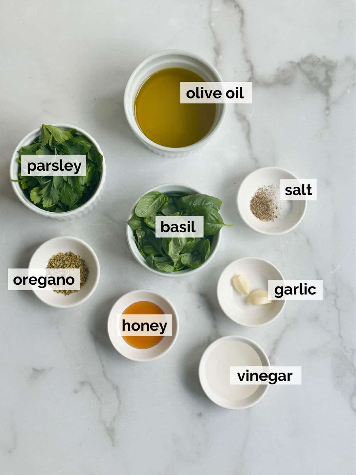 Ingredients for a Mediterranean salad dressing like parsley, basil, and garlic with olive oil on a white background. 