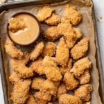Air fried chicken nuggets on a big baking sheet with a honey mustard dipping sauce.