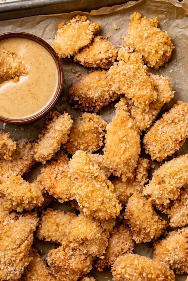 Air fried chicken nuggets on a big baking sheet with a honey mustard dipping sauce.