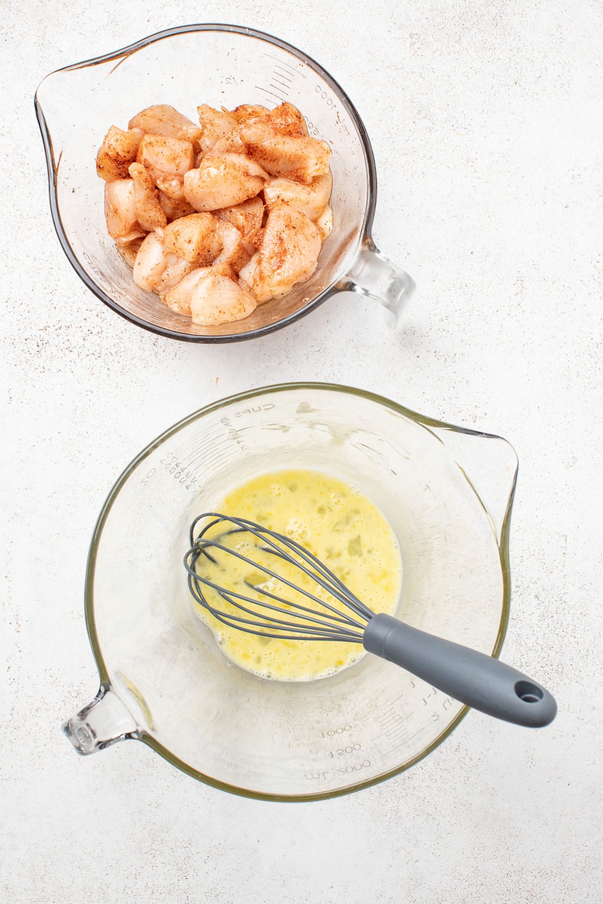 Chicken breast nuggets next to a beaten raw egg in a bowl.