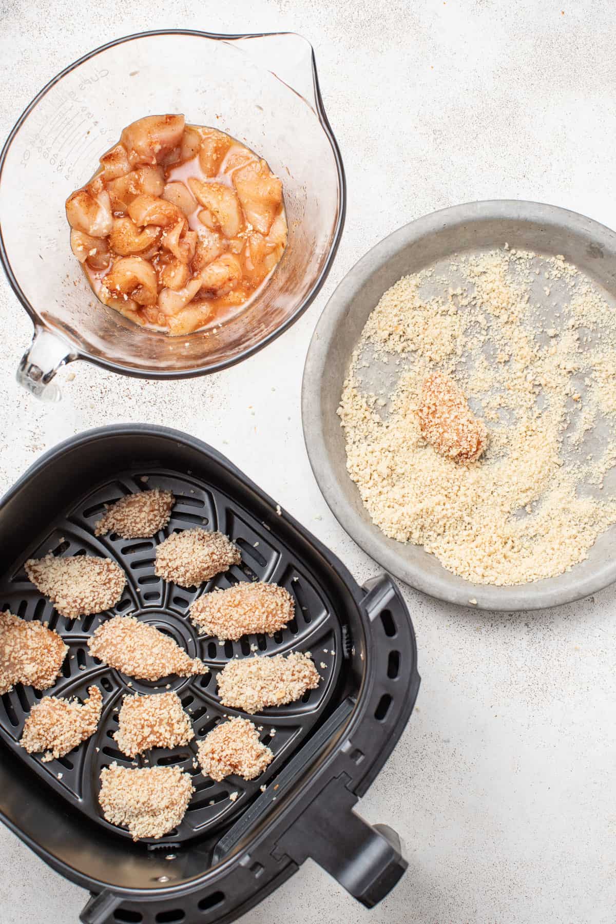 Chicken nuggets being dipped into panko and placed into an air fryer basket.