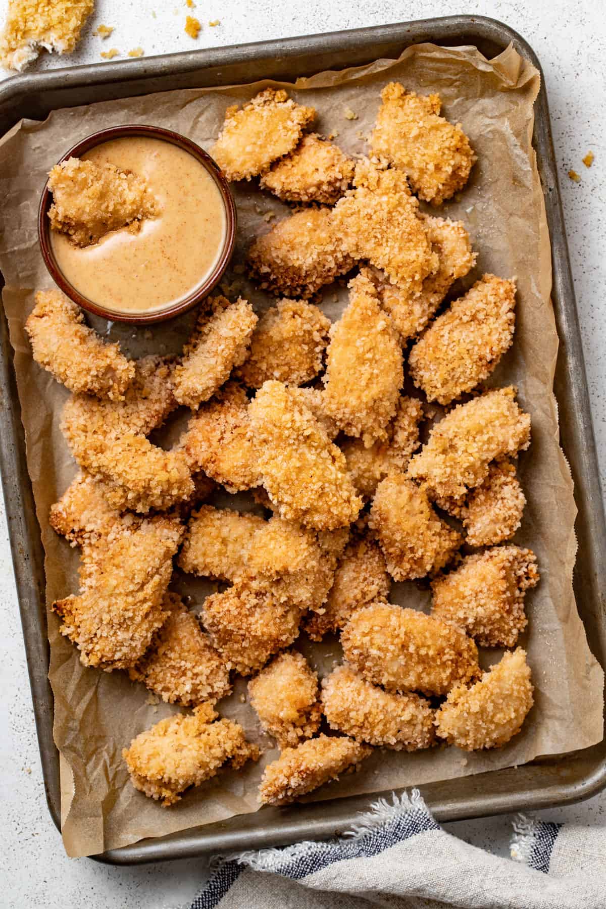 A large platter of crispy air fried chicken nuggets next to a dipping sauce.