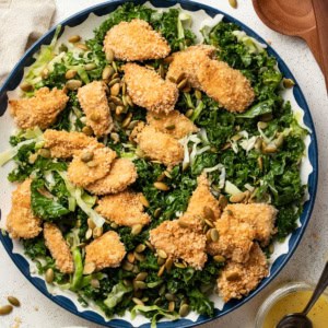 A kale crunch salad with chicken nuggets on top of it.