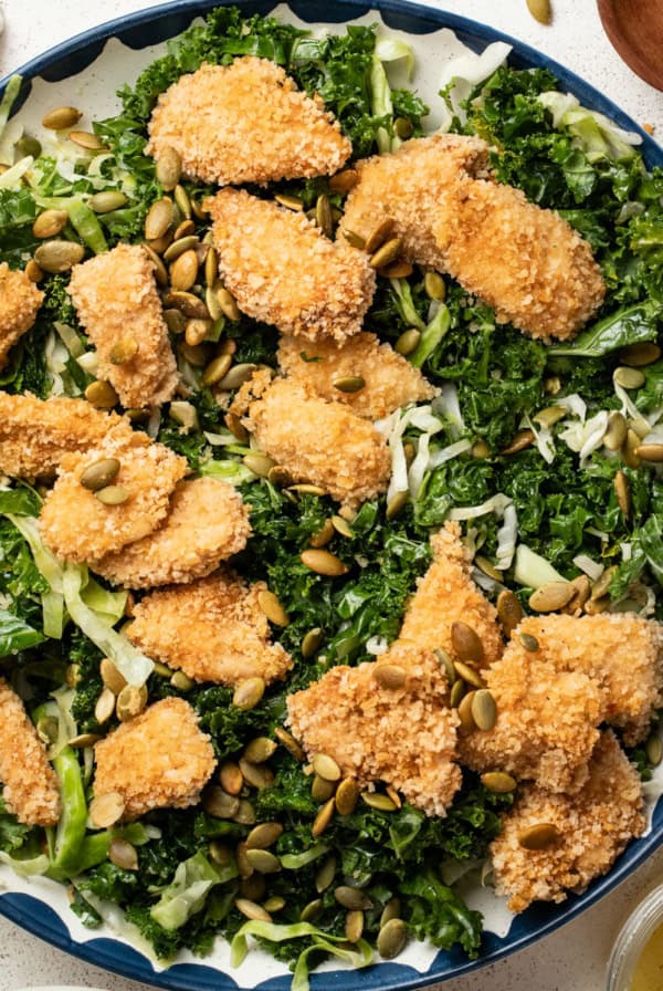 A kale crunch salad with chicken nuggets on top of it.