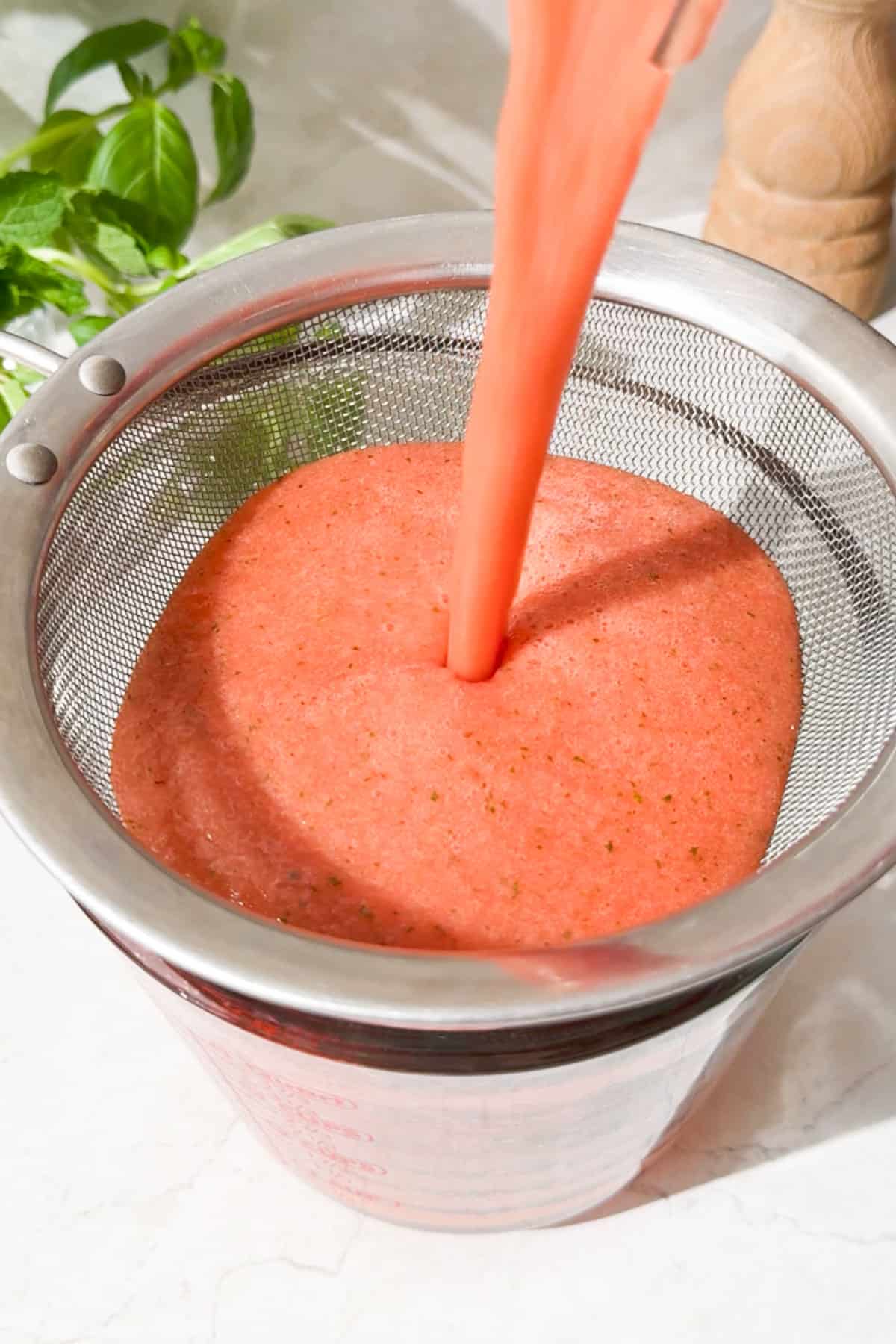 Pouring the watermelon mint juice through a strainer into a larger glass.