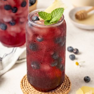 A tall glass of iced tea with blueberries, ginger and mint.