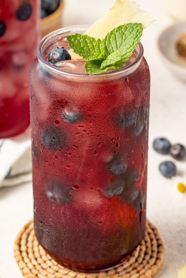 A tall glass of iced tea with blueberries, ginger and mint.