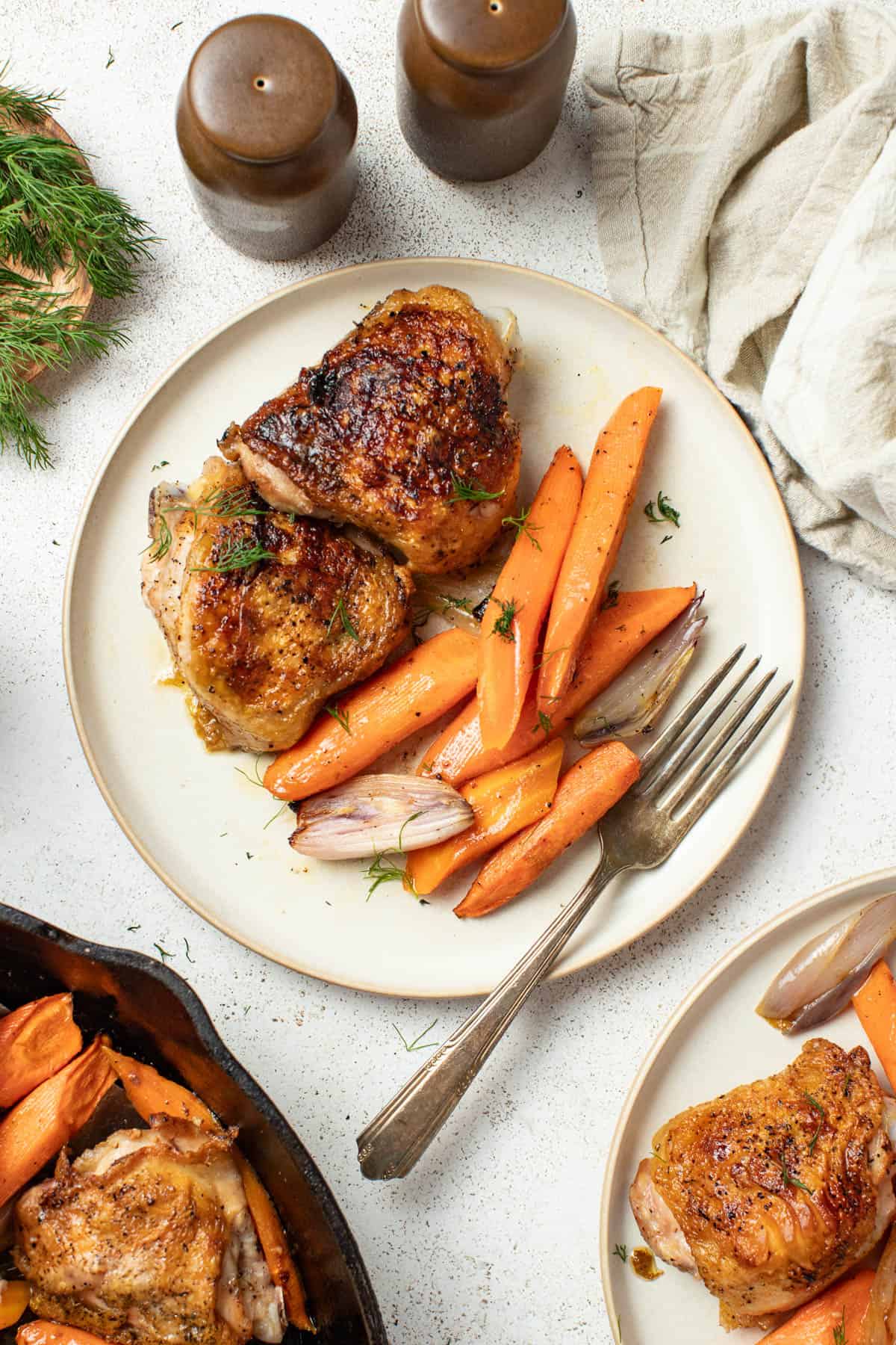 Crispy chicken thighs and carrots on a white plate with a fork.
