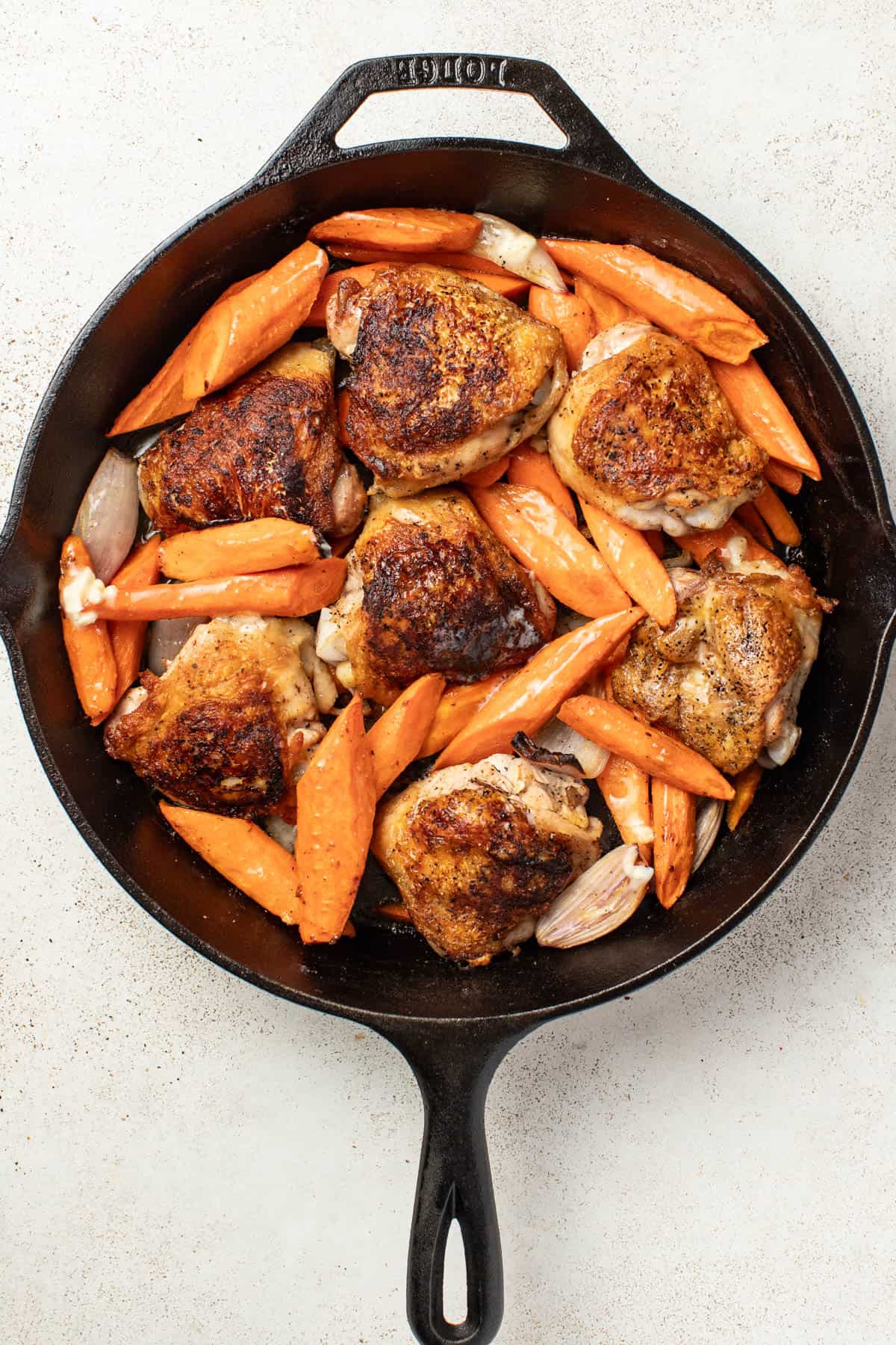 Chicken thighs with carrots and shallots in a cast iron skillet after being seared and finished cooking in the oven.