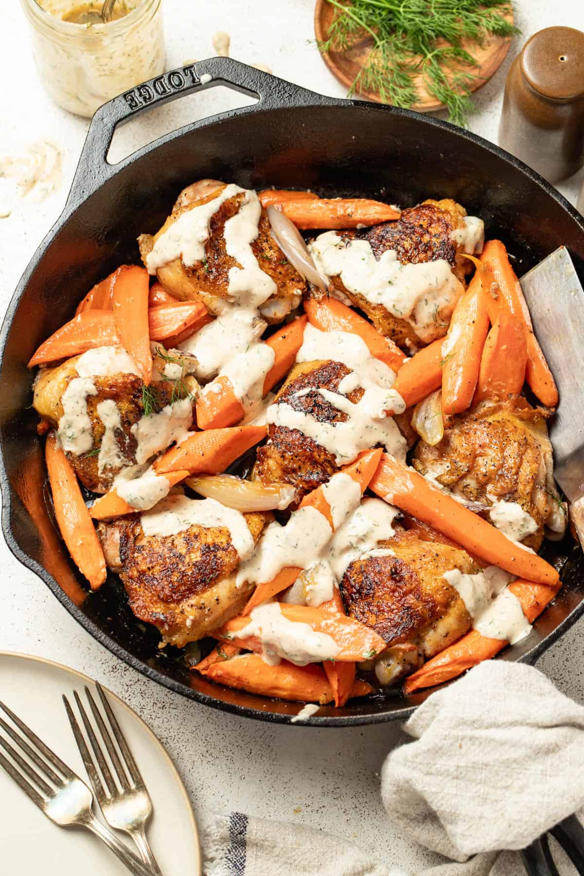 Chicken thighs and carrots in a skillet topped with a tahini sauce.