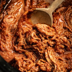 Shredded flank steak being scooped by a wood spoon in the crockpot.
