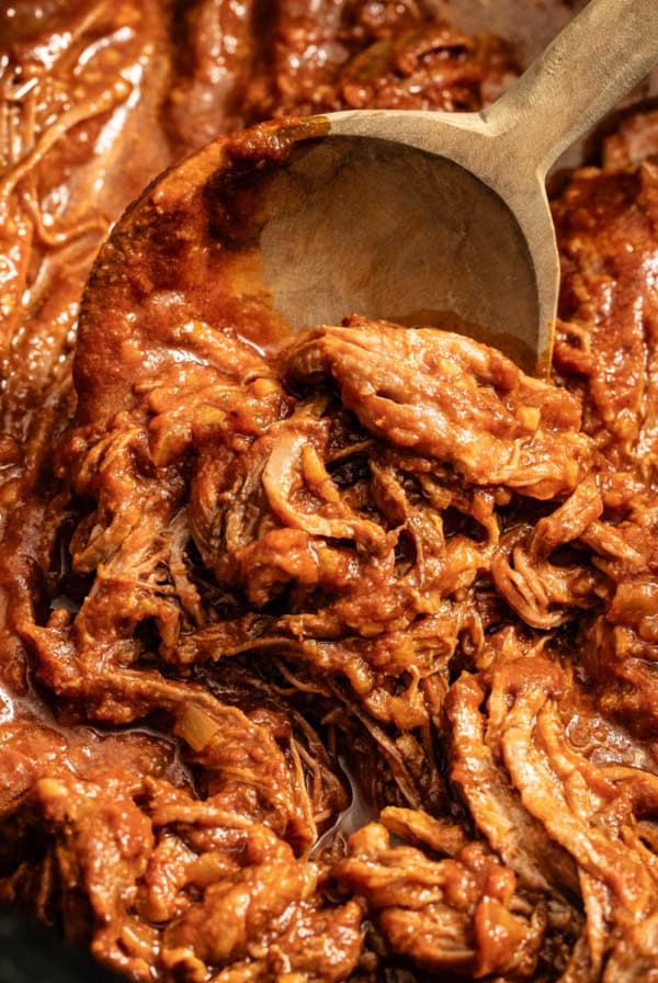 Shredded flank steak being scooped by a wood spoon in the crockpot.