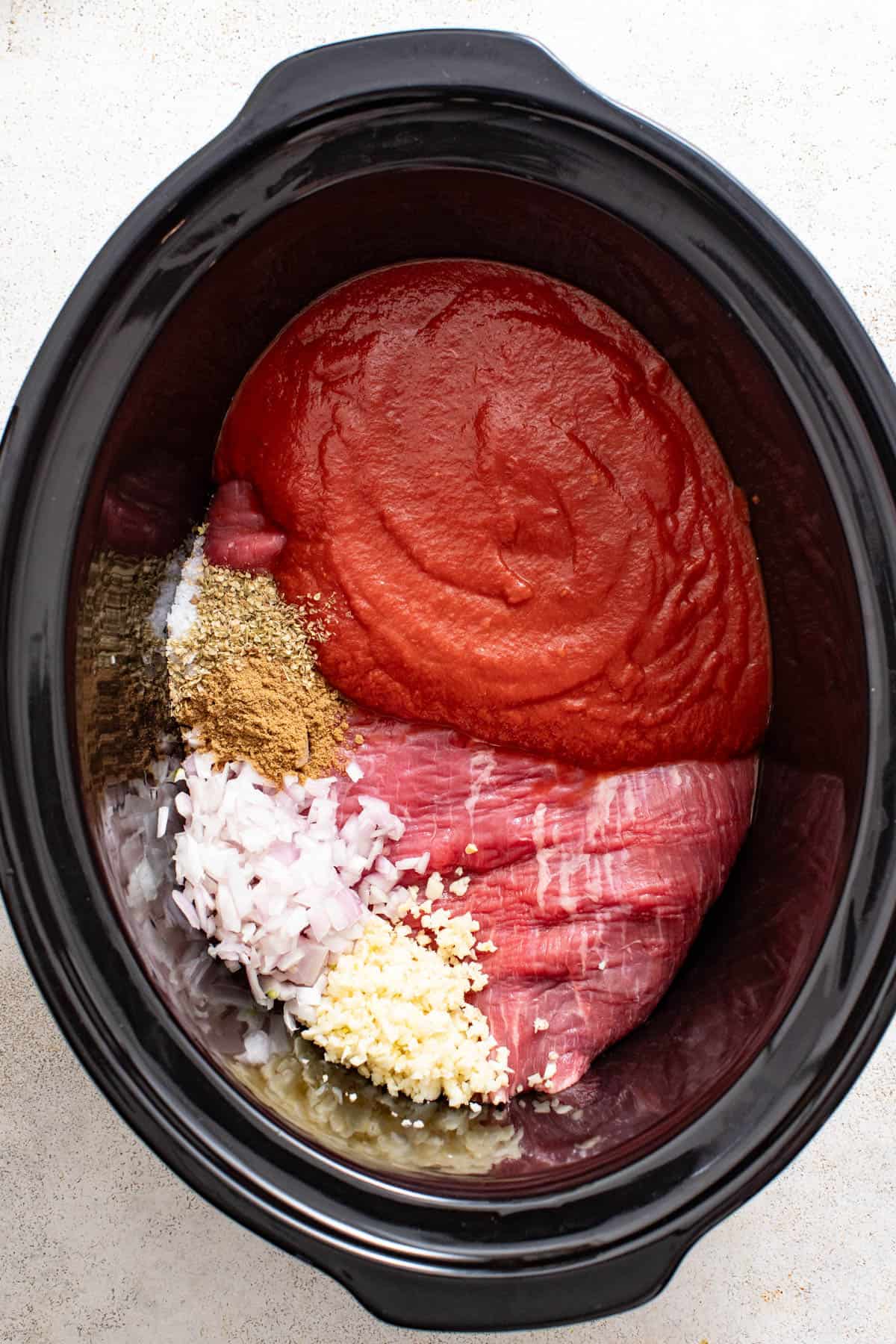 Tomatoes, flank steak, garlic and spices in a slow cooker. 