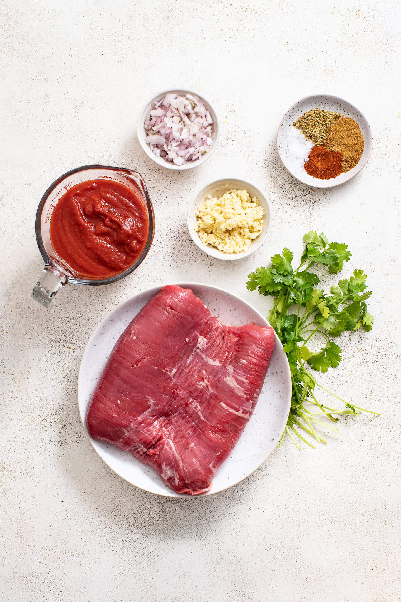 Flank steak, tomatoes, garlic and shallots on a white table. 