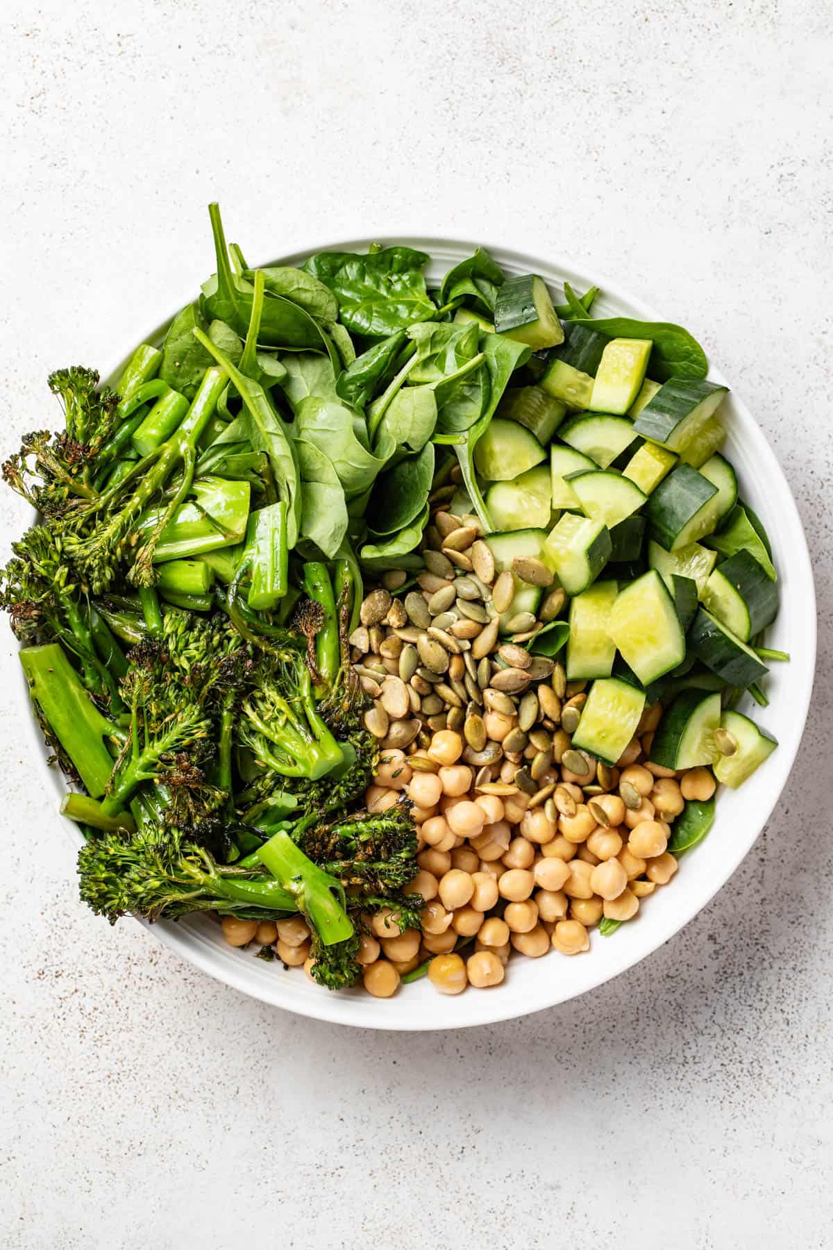 A green salad with broccolini, cucumbers, chickpeas and spinach in a large bowl.