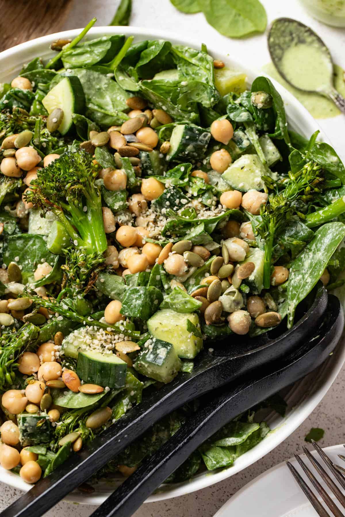 Broccolini, cucumbers and spinach in a bowl topped with pumpkin seeds.