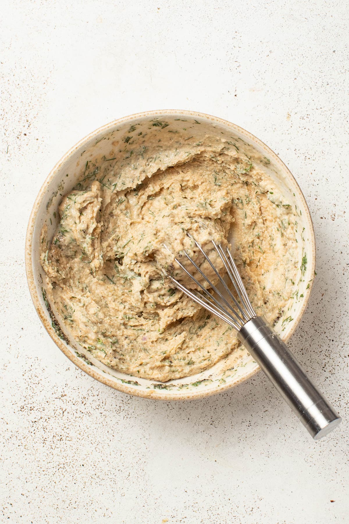 Whisking tahini, dill, vinegar, and garlic in a bowl.
