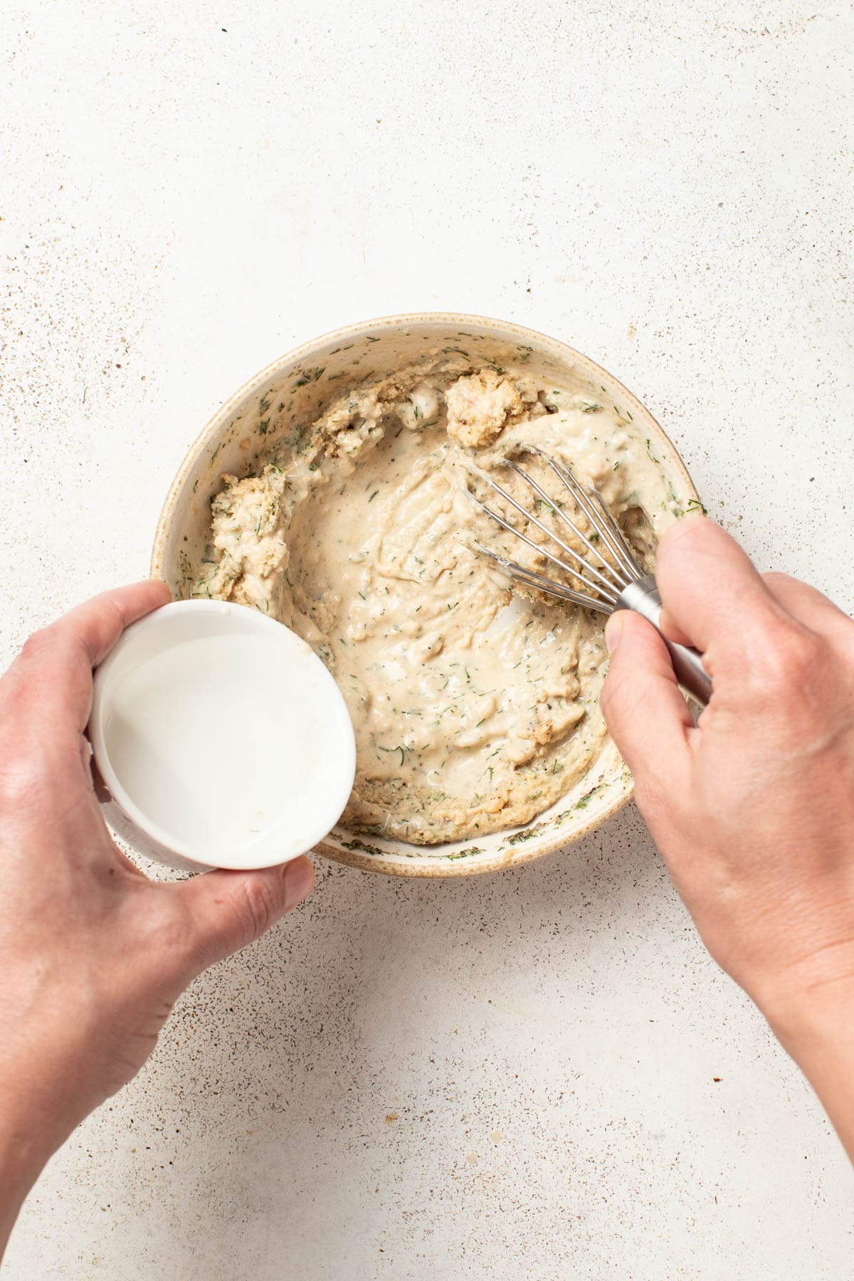 Adding warm water to a tahini sauce to thin it out.