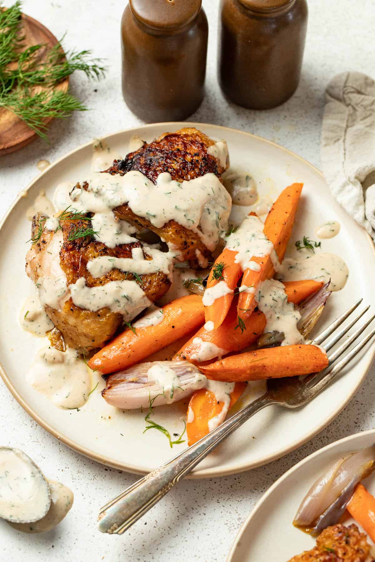 Tahini sauce drizzled on top of roasted vegetables with seared chicken thighs on a plate.