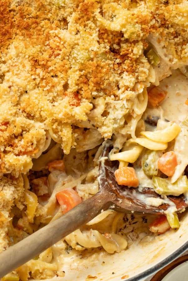 Chicken pot pie noodles on a wood spoon in a cast iron skillet.