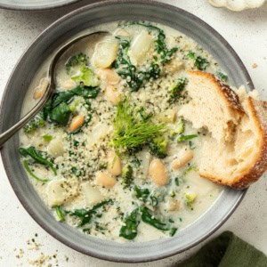 A creamy white bean soup with veggies and crusty bread dipping into it.