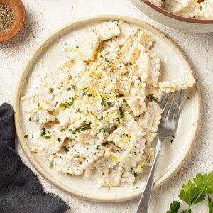 A fork digging into cream cheese pasta on a white plate.