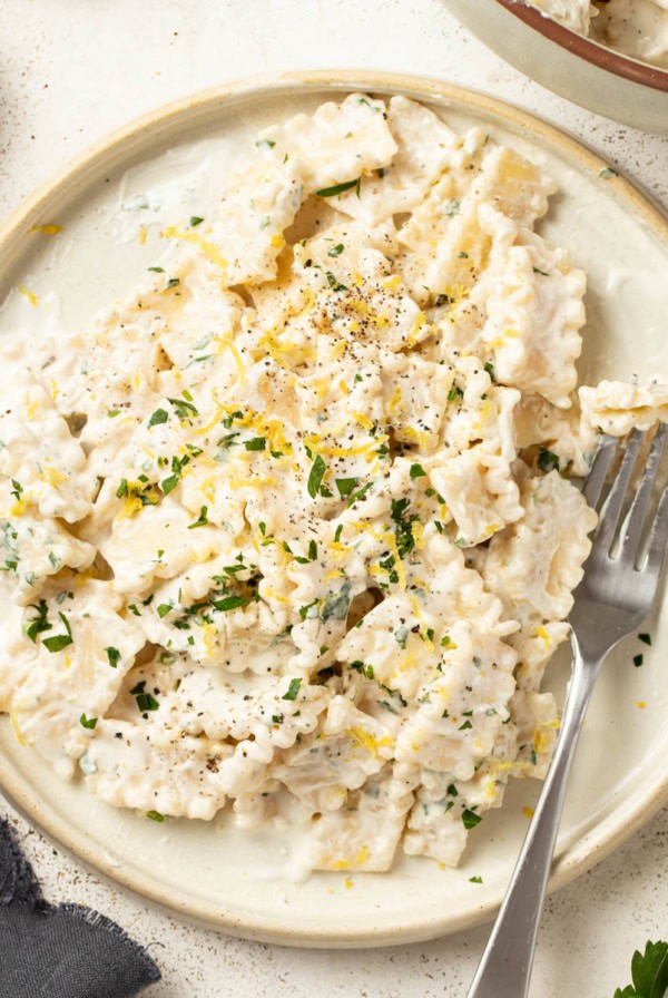 A fork digging into cream cheese pasta on a white plate.