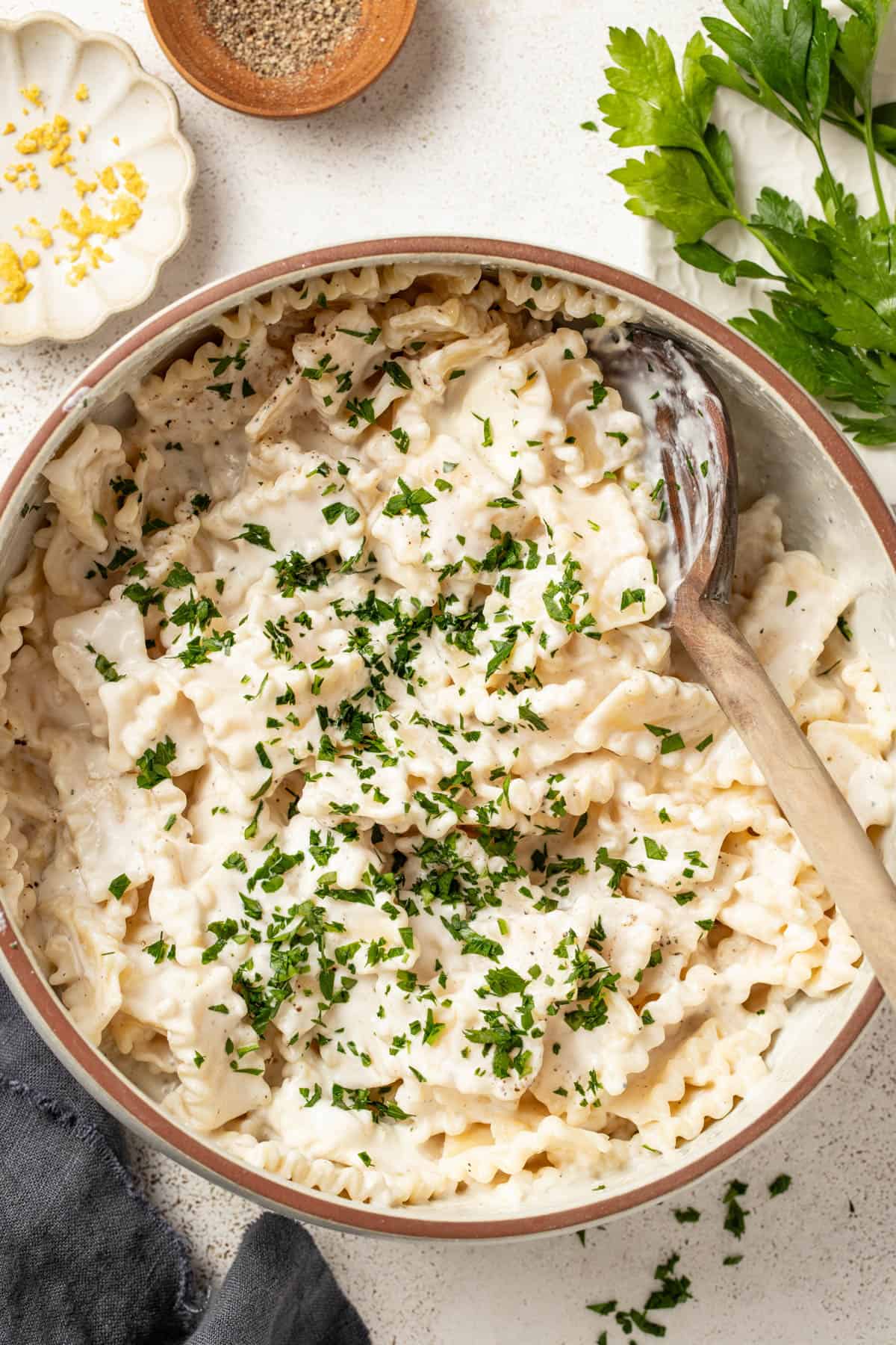 Cream cheese pasta in a big white pot with a wood spoon scooping some of the pasta.