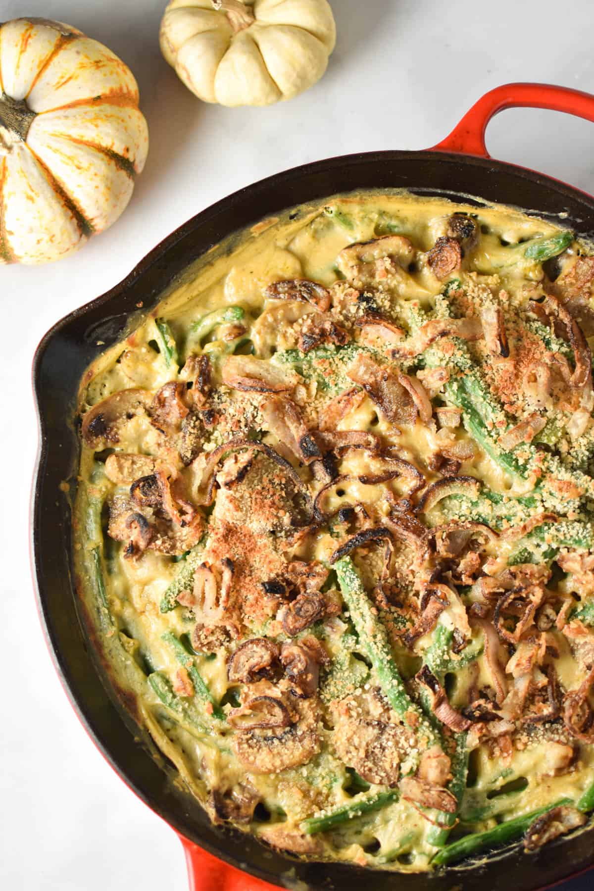 A fresh green bean casserole made without soups in a homemade mushroom sauce next to two pumpkins. 