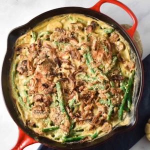 A cast iron skillet with green bean casserole made with fresh green beans and crispy shallots on top.