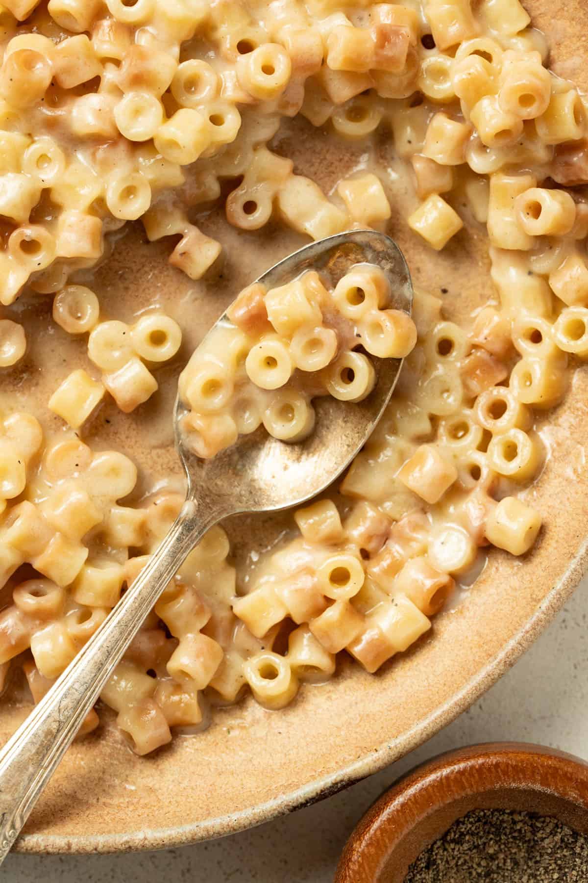 A spoon dipping into a bowl with buttered pasta noodles.