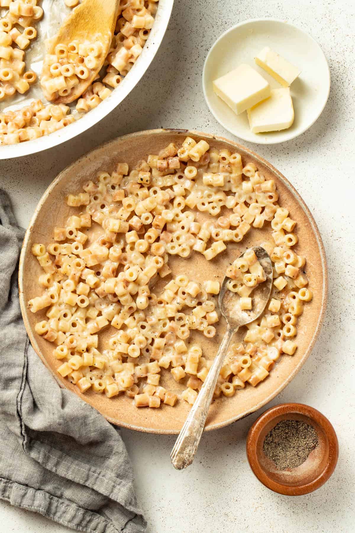 Serving the buttered pasta in a bowl next to bread and salt and pepper.