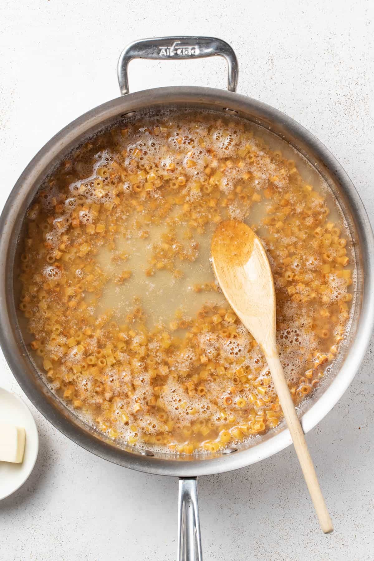 Adding broth to the skillet with the butter and pasta.